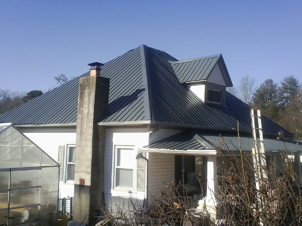Dark blue standing seam metal roof on a white farmhouse with dormer — Slate & Tile Roof Repair by Roofing Brothers in Garretson