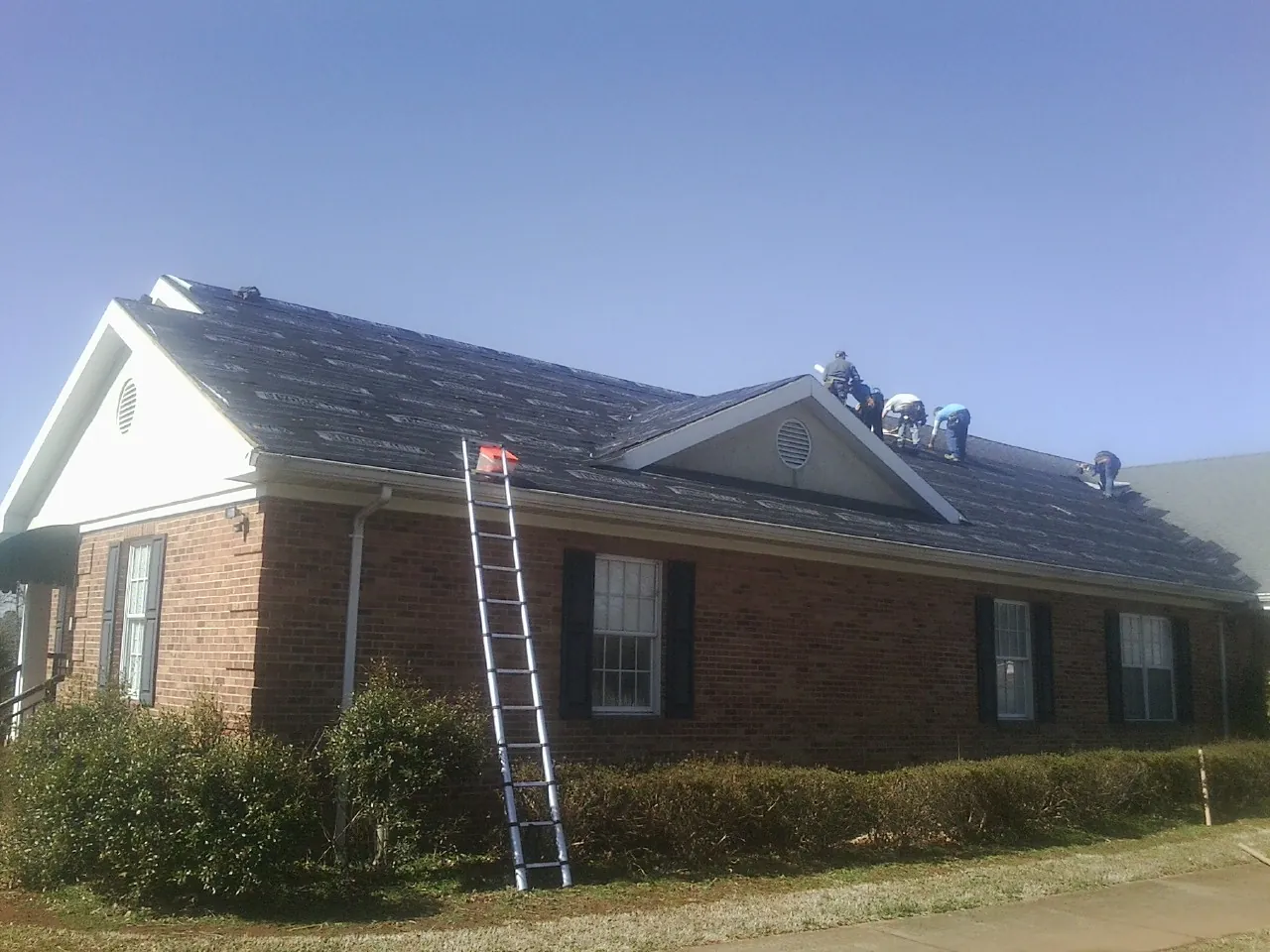Crew tearing shingles off a brick ranch roof with a ladder set — Metal Roof Repair work by our crew in Garretson