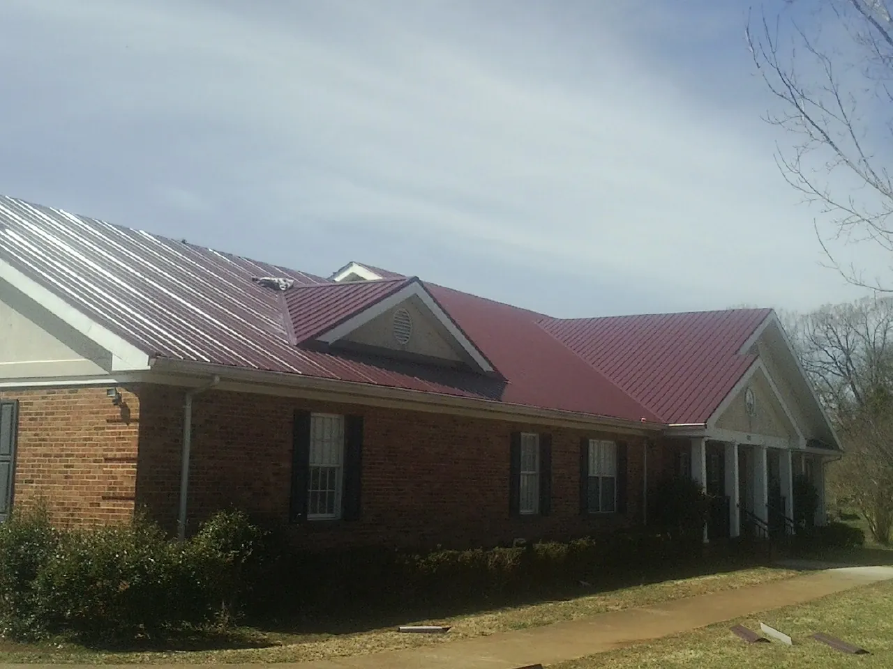 Red metal roof with gabled entries on a long brick building, from a Hail Damage Roof Repair job in Garretson