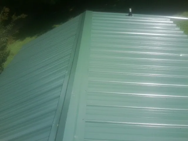 New green metal panels meeting at the ridge of a roof — Flat Roof Repair work by our crew in Garretson
