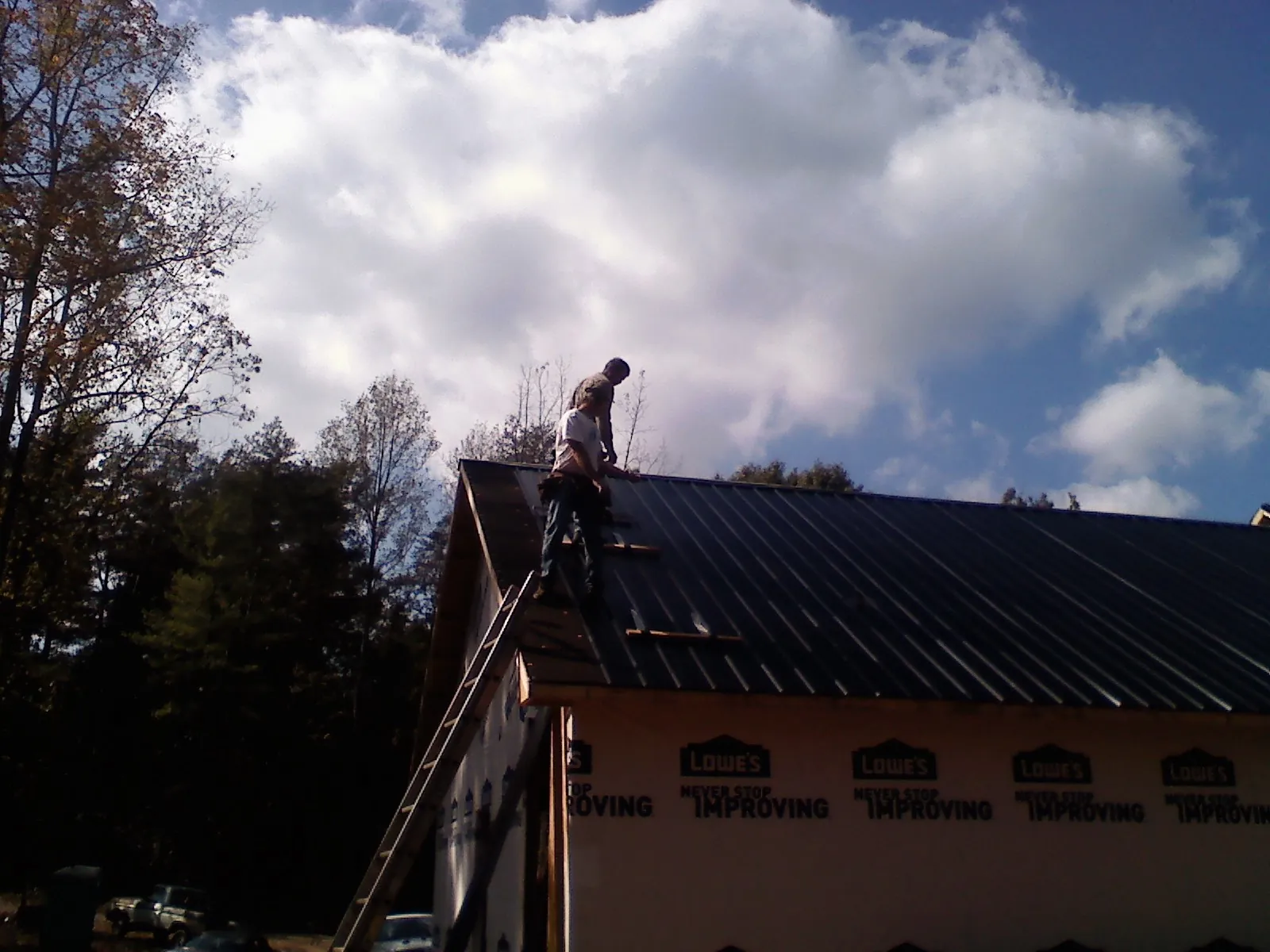 Roofer fastening dark metal panels high against a cloudy sky, from a Roof Inspection job in Garretson