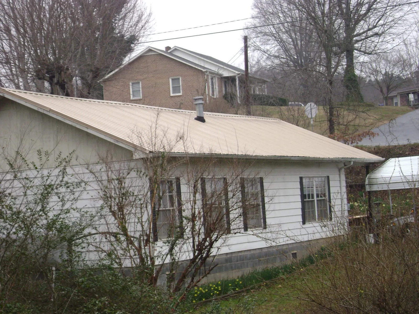 Tan metal roof on a white sided house set into a hillside — Commercial Roofing by Roofing Brothers in Garretson